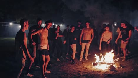 Energetic young friends dancing and celebrating around glowing bonfire, sharing vibrant nighttime moments of joy and connection during summer gathering