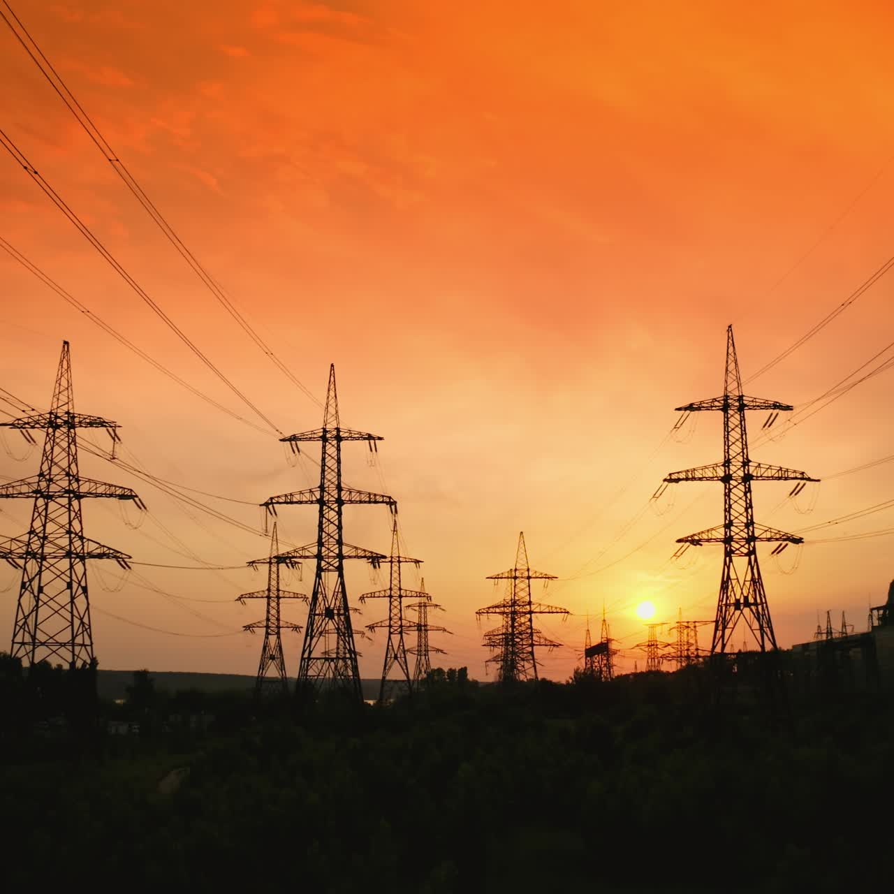 Dark silhouettes of electric towers on red sky background. Transmission lines of high-voltage electric towers at sunset