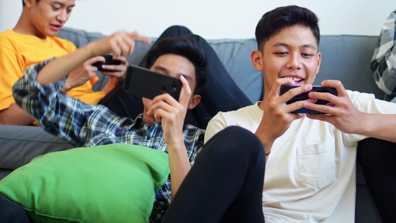 Friends Enjoy Gaming Session At Home And Focused On Their Smartphones, Highlighting Digital Leisure