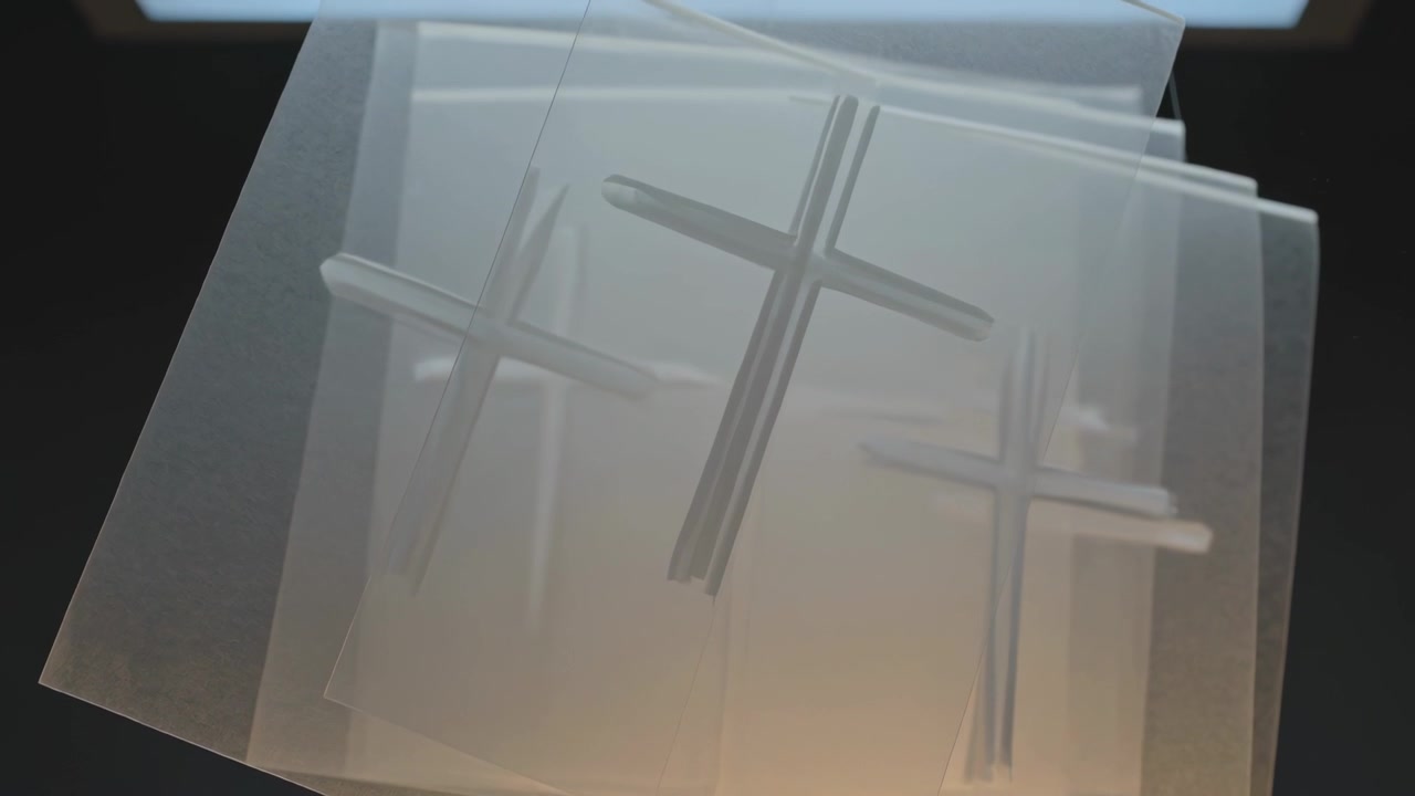 Bright light rising behind stacked sheets rotating and sliding in studio showing embossed crosses