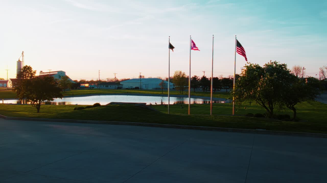 American and Ohio flags waving near pond at sunrise in quiet rural setting. Industrial setting in USA