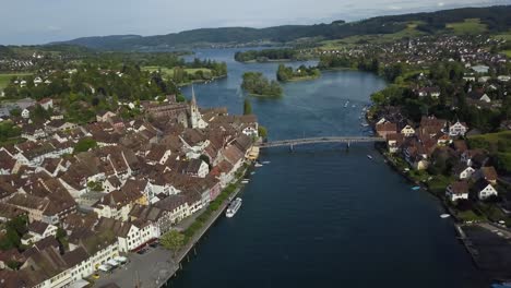 Dolly-Aéreo-En-El-Río-Rin-Y-El-Puente-En-La-Pintoresca-Ciudad-De-Stein-Am-Rhein,-Valle-Verde-Y-Colinas-En-El-Fondo,-Suiza