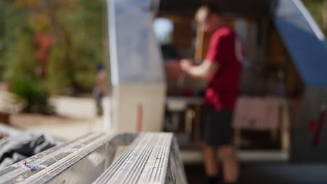 A-hand-grabs-a-carpenters-square-as-a-construction-worker-builds-a-travel-trailer-in-the-background-with-copy-space