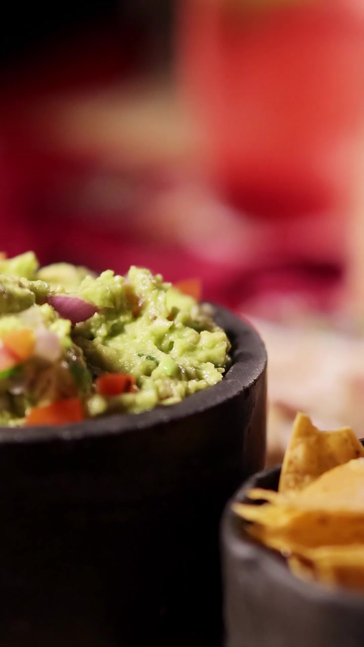 Primo piano di guacamole e patatine in un vivace ambiente da ristorante con illuminazione calda e arredamento colorato.