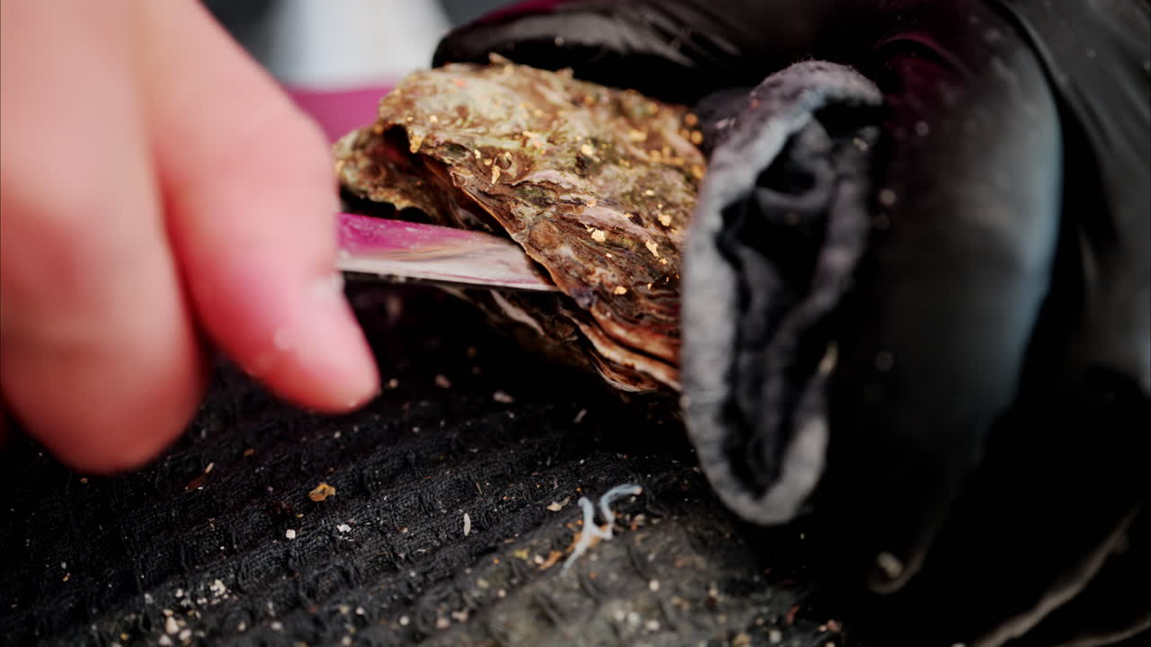 Close up of a waiter opening up a raw oyster at a restaurant