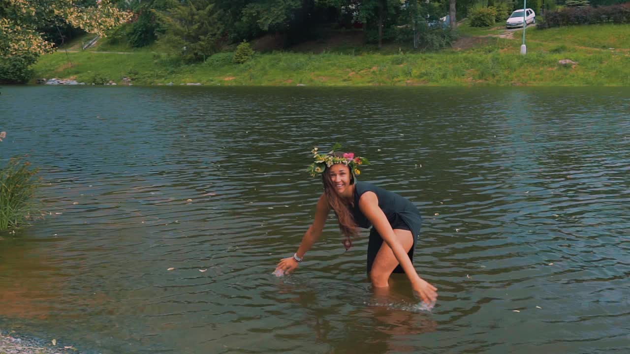 물에서 하늘로 손을 올리는 머리에 드레스와 꽃 화환을 입은 맨발의 소녀 슬로우 모션