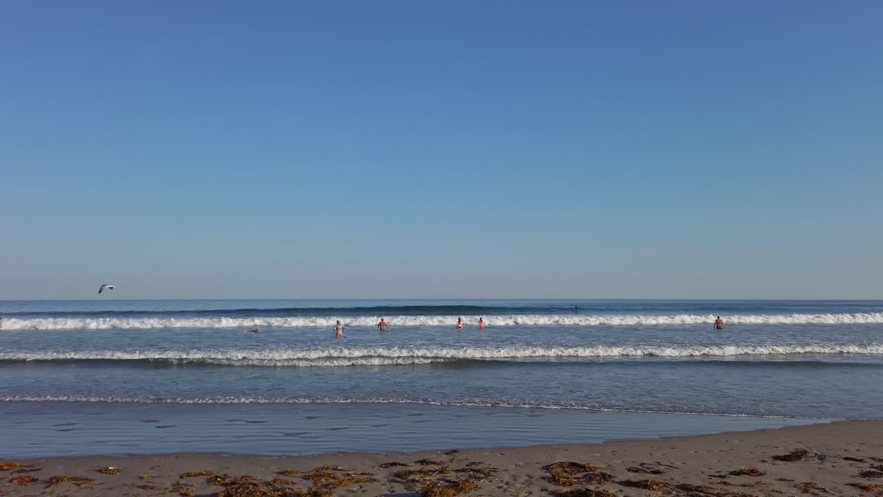 People enjoying Atlantic ocean's water and waves on Singing beach in Massachusetts at sunset. Bottom view from shore