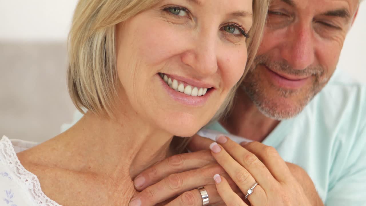 pareja casada abrazándose y sonriendo a la cámara en la cama juntos