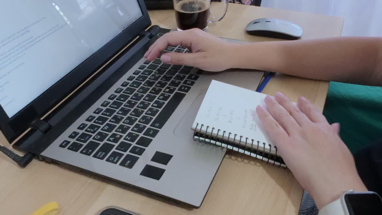 Person combining traditional note-taking in a spiral notebook with digital work on a laptop.
