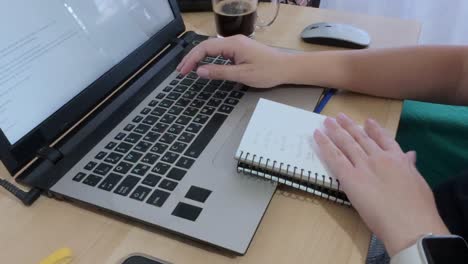 person combining traditional note-taking in a spiral notebook with digital work on a laptop.
