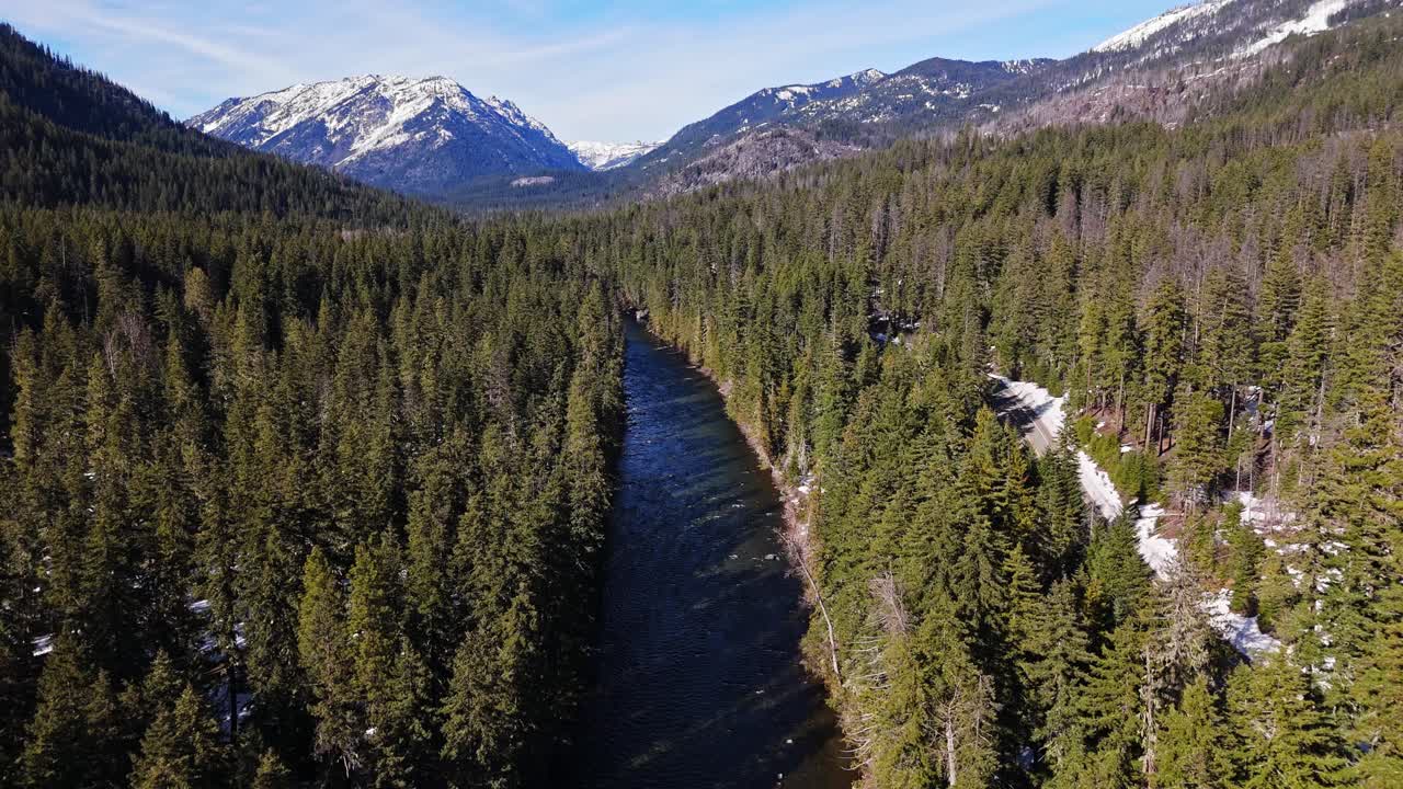 Backwards scenic shot of river and Evergreen forest with snow capped mountains in the background in Cle Elum on a clear day in Washington State