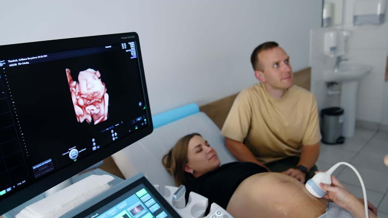Pregnant Caucasian lady is having ultrasonic check up. Baby image is on the black screen of the machine.