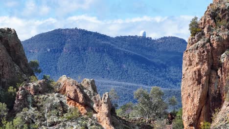 camera slowly pans right across rugged sandstone cliffs and bushland, revealing distant observatory domes under bright daylight in warrumbungle national park