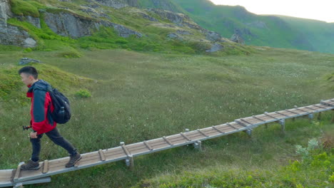 siguiente toma de un joven asiático caminando por un sendero de madera con un trípode
