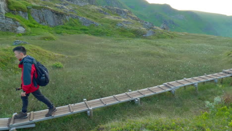 following shot of an asian young male walking on wooden trail with a tripod