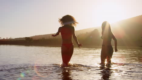 female friends on vacation wading out into a lake at sundown