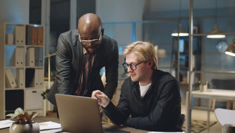 multiethnic businessmen discussing project on laptop in office at night