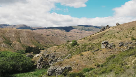 Felsige-Hügel-Neuseelands-Unter-Einem-Teilweise-Bewölkten-Himmel-Mit-Viel-Grün-Und-Vereinzelten-Sträuchern