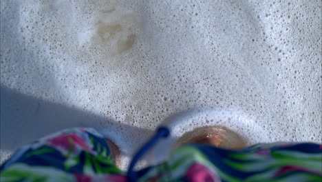 Slow-motion-POV-of-a-suntanned-man-standing-on-the-sand-at-a-caribbean-beach-getting-washed-by-the-waves-in-Cancun-Mexico