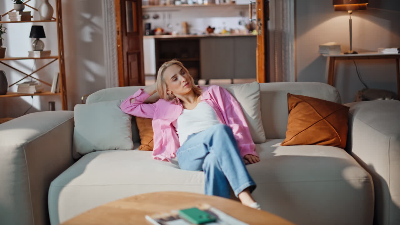 Satisfied blonde taking sit on couch stroking cushions at stylish lounge space