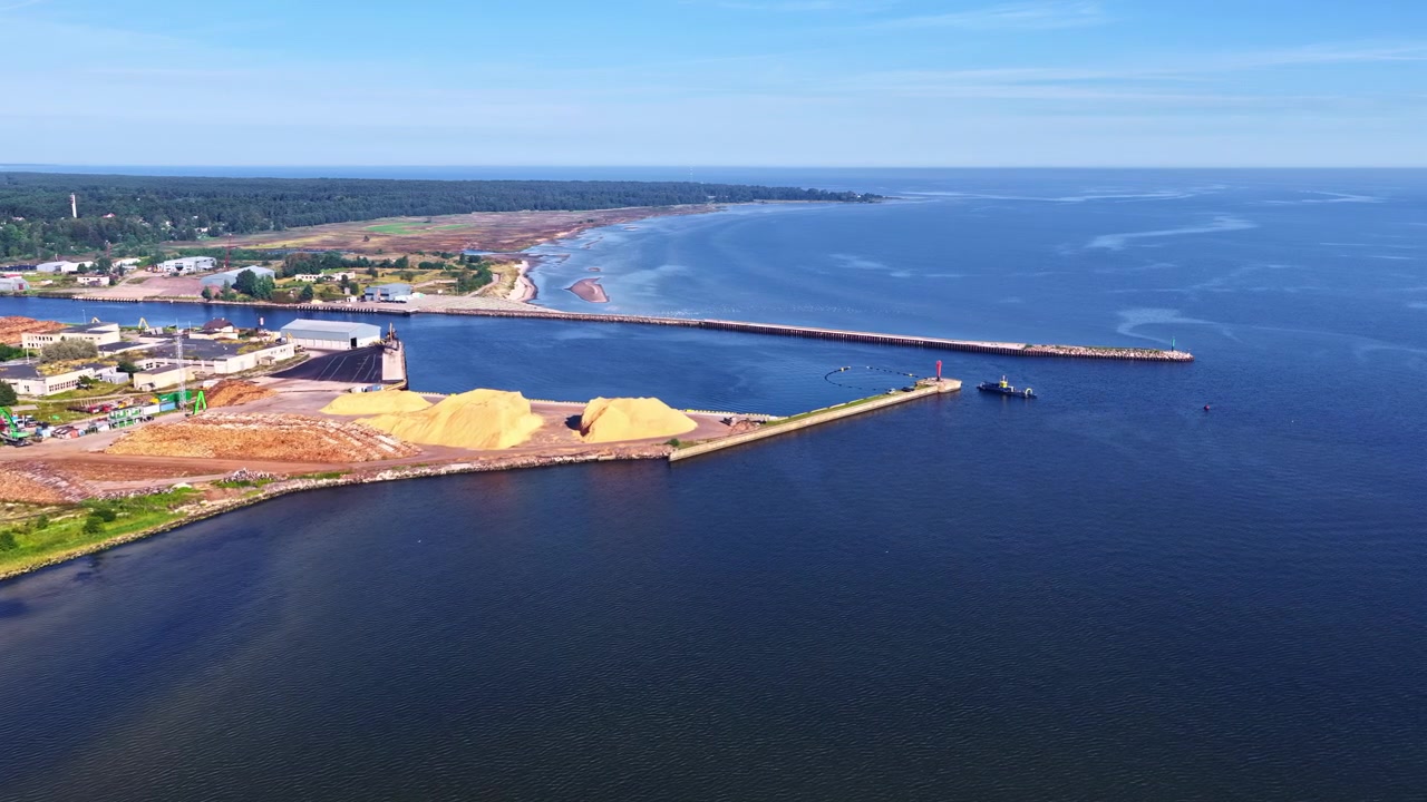 Flygvy över en kusthamn med vågbrytare, blått hav, kustlinje och hamnområde.