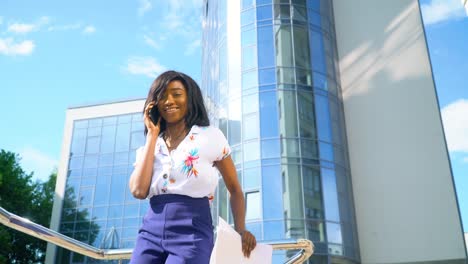 adult african american young businesswoman is talking on phone outside near modern office building
