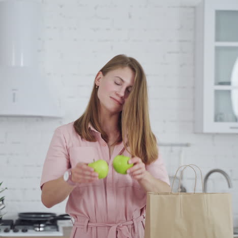 beautiful woman holding green apples on kitchen background. happy female closing her eyes by two fresh apples indoors. dieting concept.
