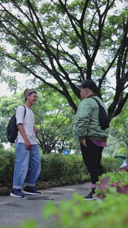 two friendly asian male students chatting while standing in campus park
