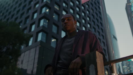 Black-afro-American-guy-low-angle-locking-in-to-camera-with-modern-smart-city-skyline-in-background-illuminated-at-night