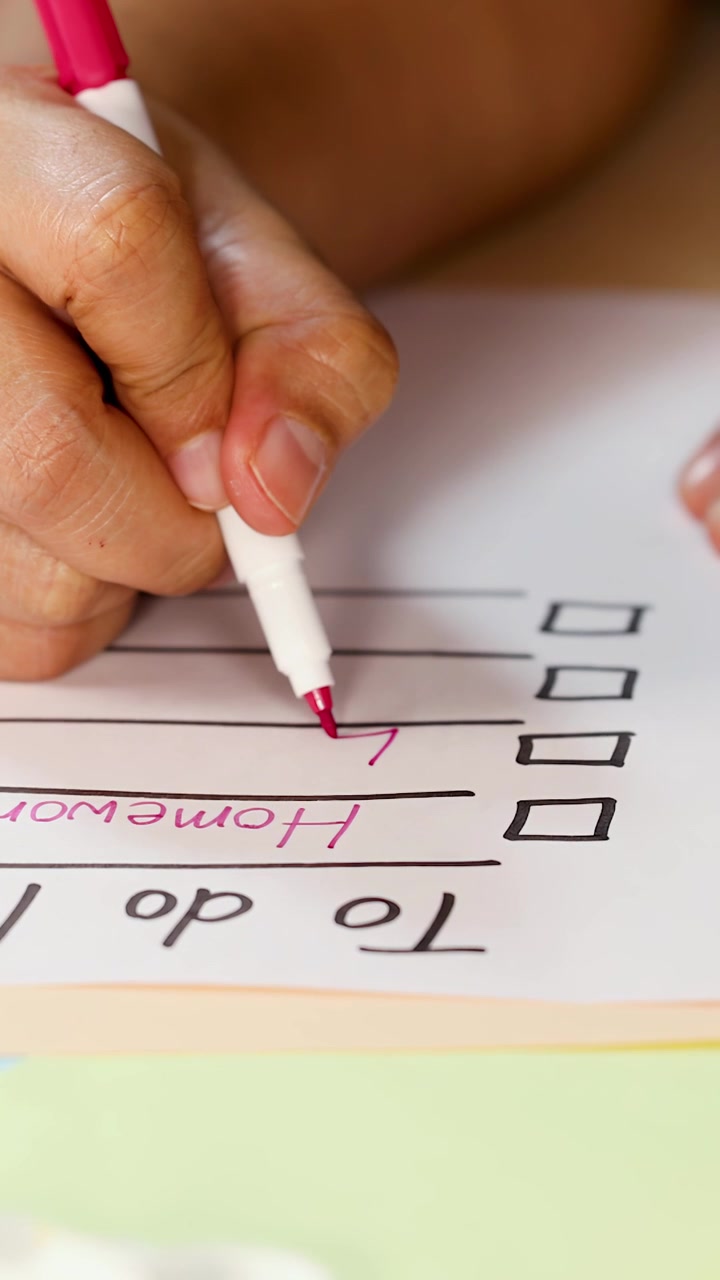 Una persona scrive compiti su una checklist di carta usando un pennarello rosa, primo piano, illuminazione naturale, telecamera fissa.