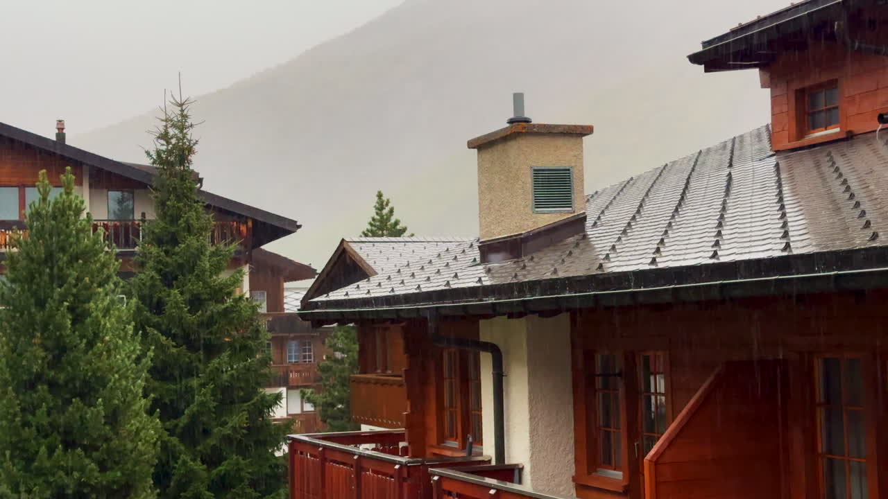 Swiss alps heavy rainy rain windy alpine valley chalet two buildings  moody cloudy gray grey morning Swiss alps Saas Fee Zermatt Saastal ski resort downtown Switzerland Europe slow motion static shot