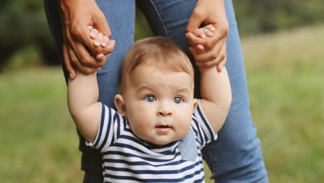 close up of a baby boy taking his first steps in the grass while holding his mother's hands