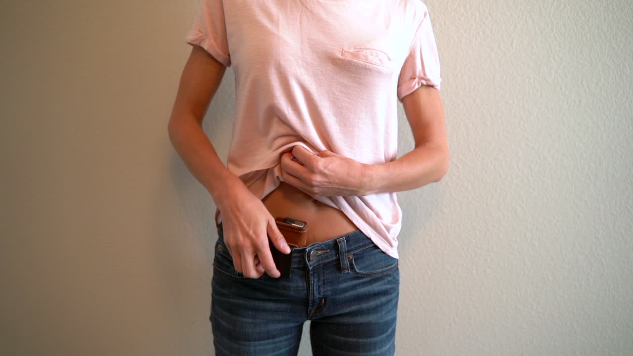 그녀의 셔츠를 풀고 그녀의 허리선에서 그녀의 숨겨진 홀스터 총을 제거하는 여성의 슬로우 모션