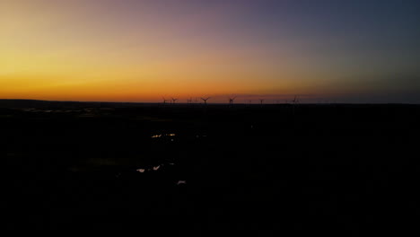 aerial shot - flying away from the wind farm on sunset, wind turbines silhouette far away on background, puck, pomorskie, poland