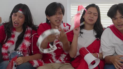 sad disappointed group of indonesian supporters watching their football team losing the match on tv