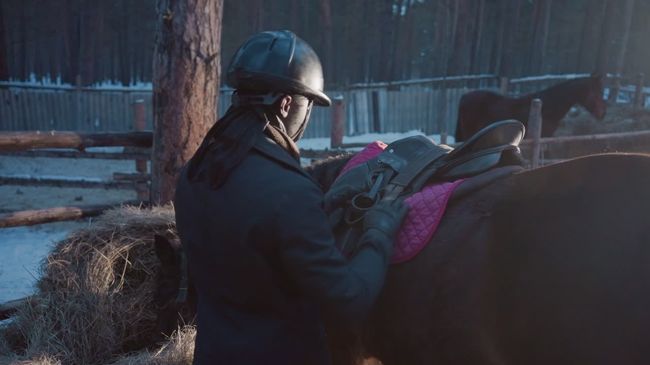 Adamın atın üzerine eyer yerleştirmesi, adam ve bakıcının eyer yerleştirdiği zorlu çiftlik sahnesi, ekip çalışmasıyla eyer yerleştirmeyi sergileyen rustik çiftlik ortamı ve karlı çevre