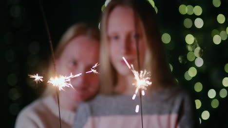 Mom-and-daughter-are-burning-sparklers-on-the-background-of-the-Christmas-tree-at-home