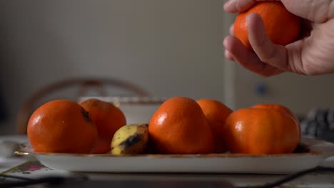 Saftige-Satsumas,-Die-Von-Der-Hand-Eines-Mannes-Von-Einem-Teller-Abgeholt-Werden,-Nahaufnahme