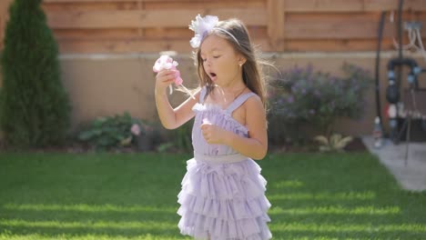 a little girl in a dress is blowing soap bubbles in the backyard on a sunny summer day