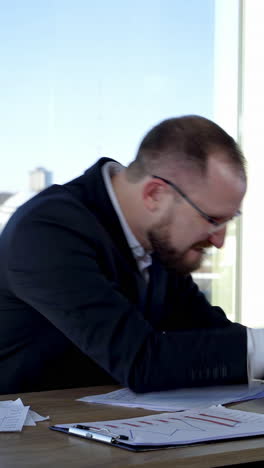 funny businessman typing on a laptop. office worker in glasses sitting at his desk in workplace and making mad face. problems in business. vertical video