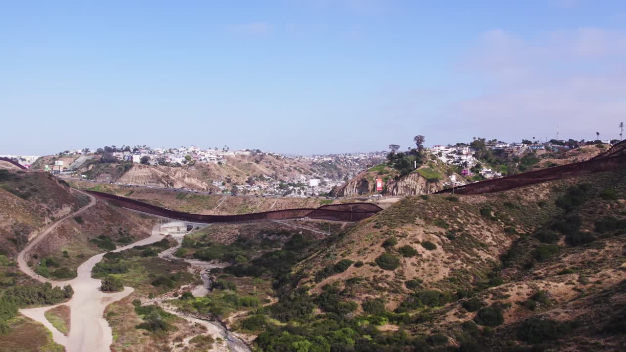 Aerial view of the border wall cutting through a valley, separating urban Tijuana from the open desert of southern California.