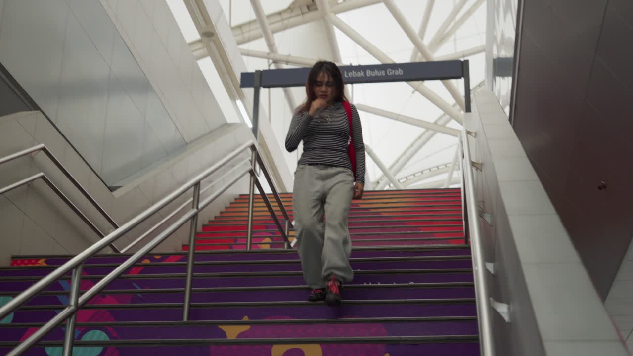 Young woman in casual clothing hurries down colorful subway stairs with a modern urban backdrop