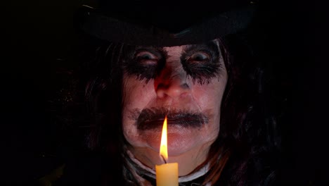 sinister woman with scary halloween witch makeup in costume making voodoo magic rituals with candle