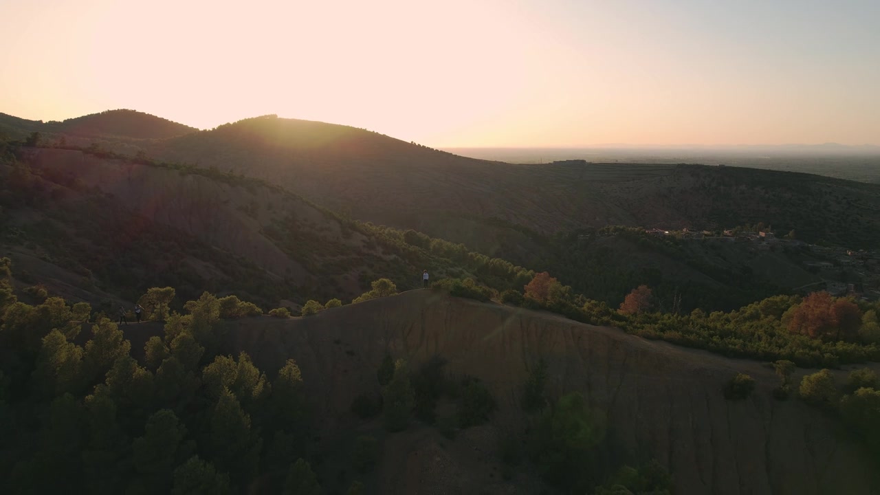 Punggung bukit berhutan di atas Lembah Ourika, Provinsi Al Haouz, Marrakesh-Safi, Maroko, disinari matahari rendah melintasi kaki bukit High Atlas dan hutan, pengambilan gambar drone menurun