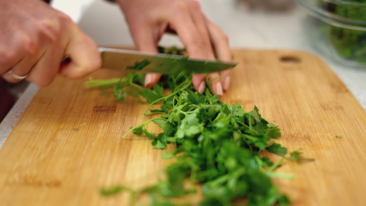 Close up of a woman cutting up parsley on a wooden board