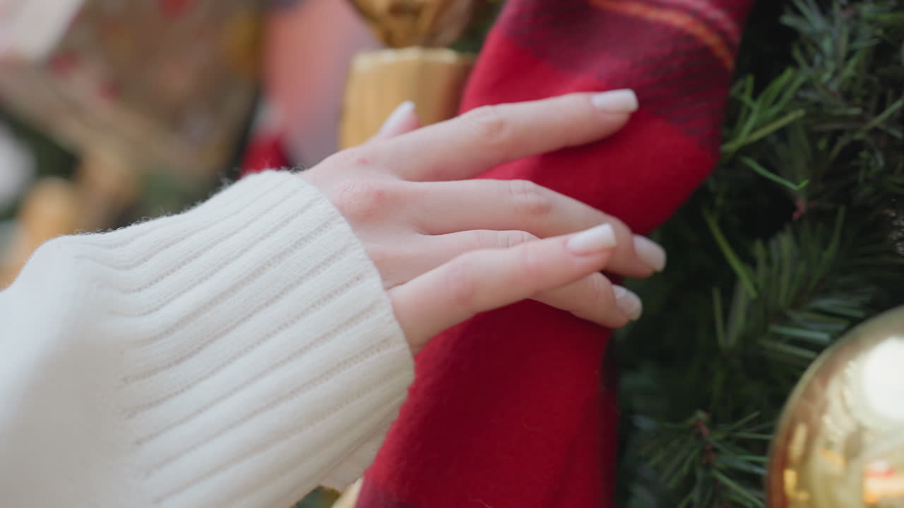Close-up of woman hand in white sleeve gently touching large Christmas tree ornament, with festive tree decorations in soft focus and holiday spirit in the background