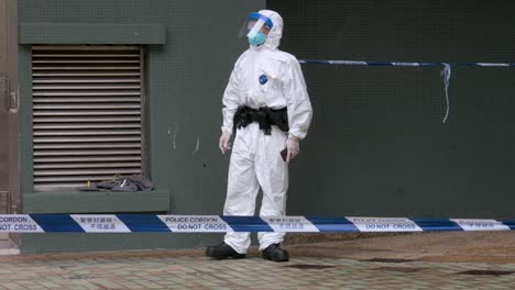un oficial de policía con un traje de protección personal frente a una cinta de cordón se para fuera de un edificio bloqueado después de que una gran cantidad de residentes dieron positivo en hong kong