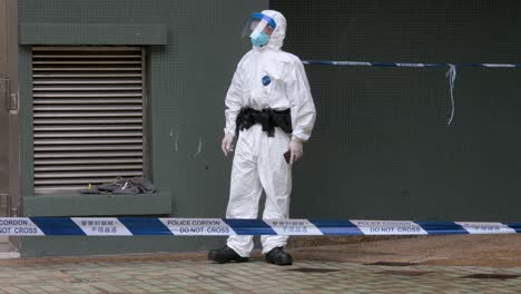 a police officer wearing a ppe suit in front of a cordon tape stands outside a building placed under lockdowncafter a large number of residents tested positive in hong kong