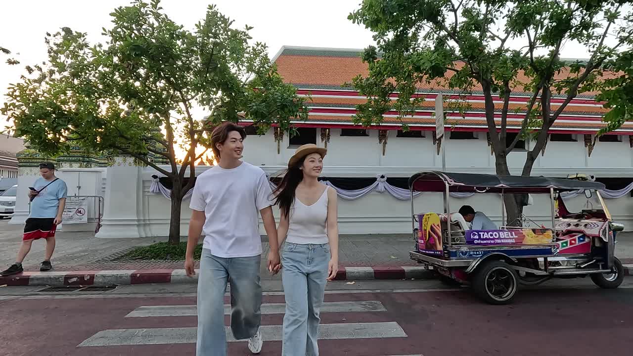 Romantic couple walks hand in hand across city crosswalk near temple at sunset