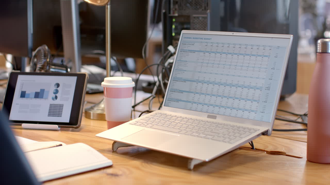 A laptop displays a detailed business budget spreadsheet in an office setting